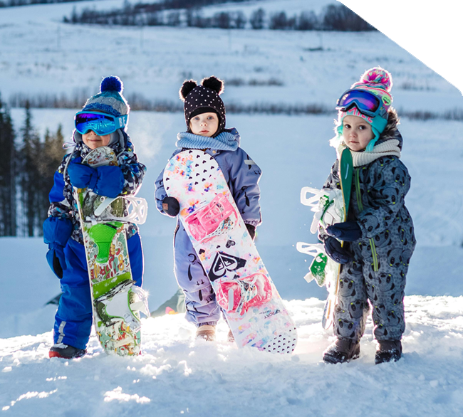 Three young children in winter gear holding colorful snowboards at a snowy Mt Buller